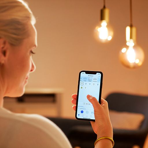 Eine Frau hält ein Telefon mit einer App-Oberfläche, im Hintergrund zwei Glühbirnen.