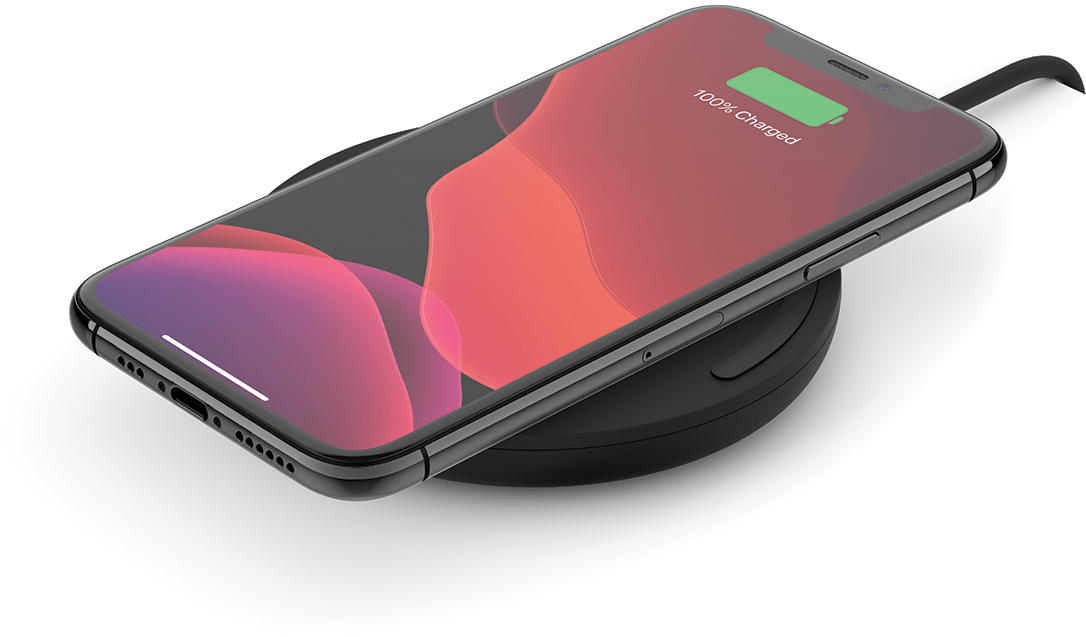 Zwarte telefoon op een oplaadpad, scherm toont 100% opgeladen. Zwarte kabel bevestigd. Witte achtergrond.