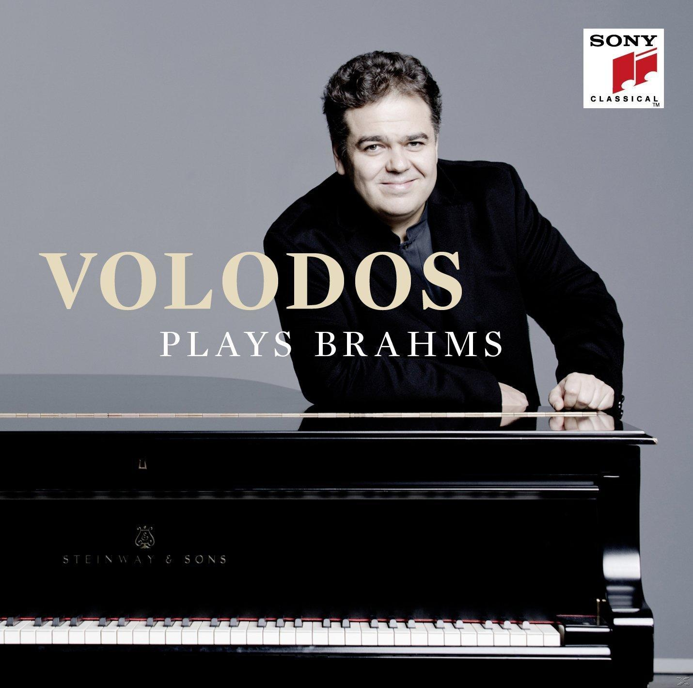 Egy öltönyös férfi egy fekete zongorára támaszkodik. A 'Volodos Plays Brahms' cím.