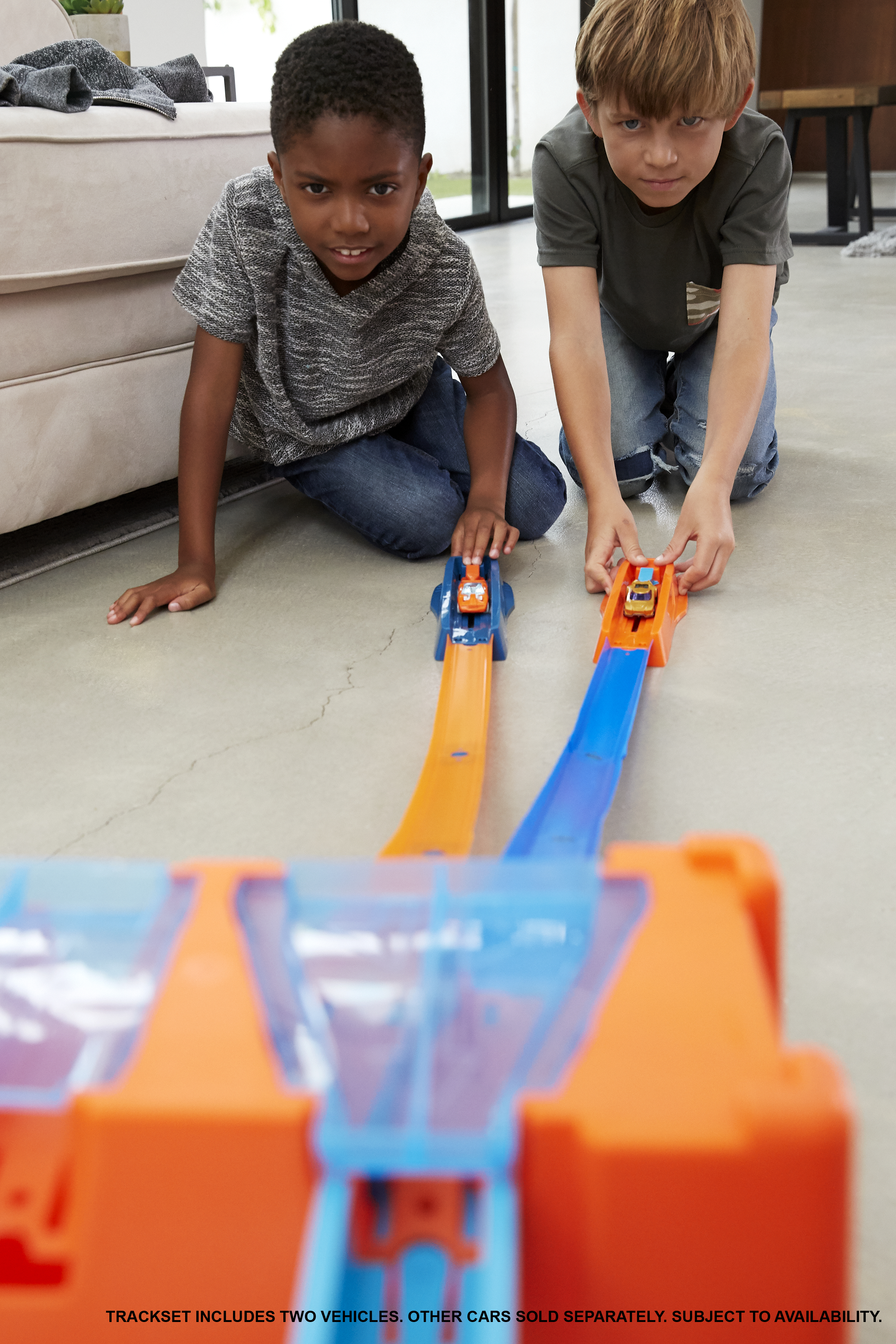 Zwei Jungen knien und spielen mit Spielzeug-Rennwagen auf Rennstrecken. Die Strecke ist orange und blau.