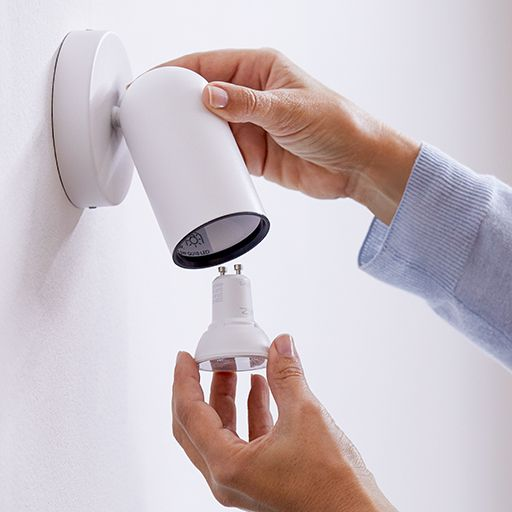 Hände, die eine Glühbirne in eine weiße, an der Wand befestigte Lampe einsetzen.