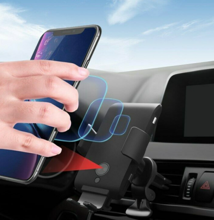 Egy kéz egy okostelefont helyez egy fekete autós telefontartóra, kék ég a háttérben.