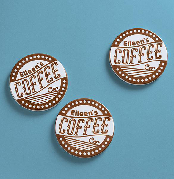 Drei runde Untersetzer mit 'Eileen's Coffee' auf blauem Hintergrund. Braunes und weißes Design mit Punkten und Linien.