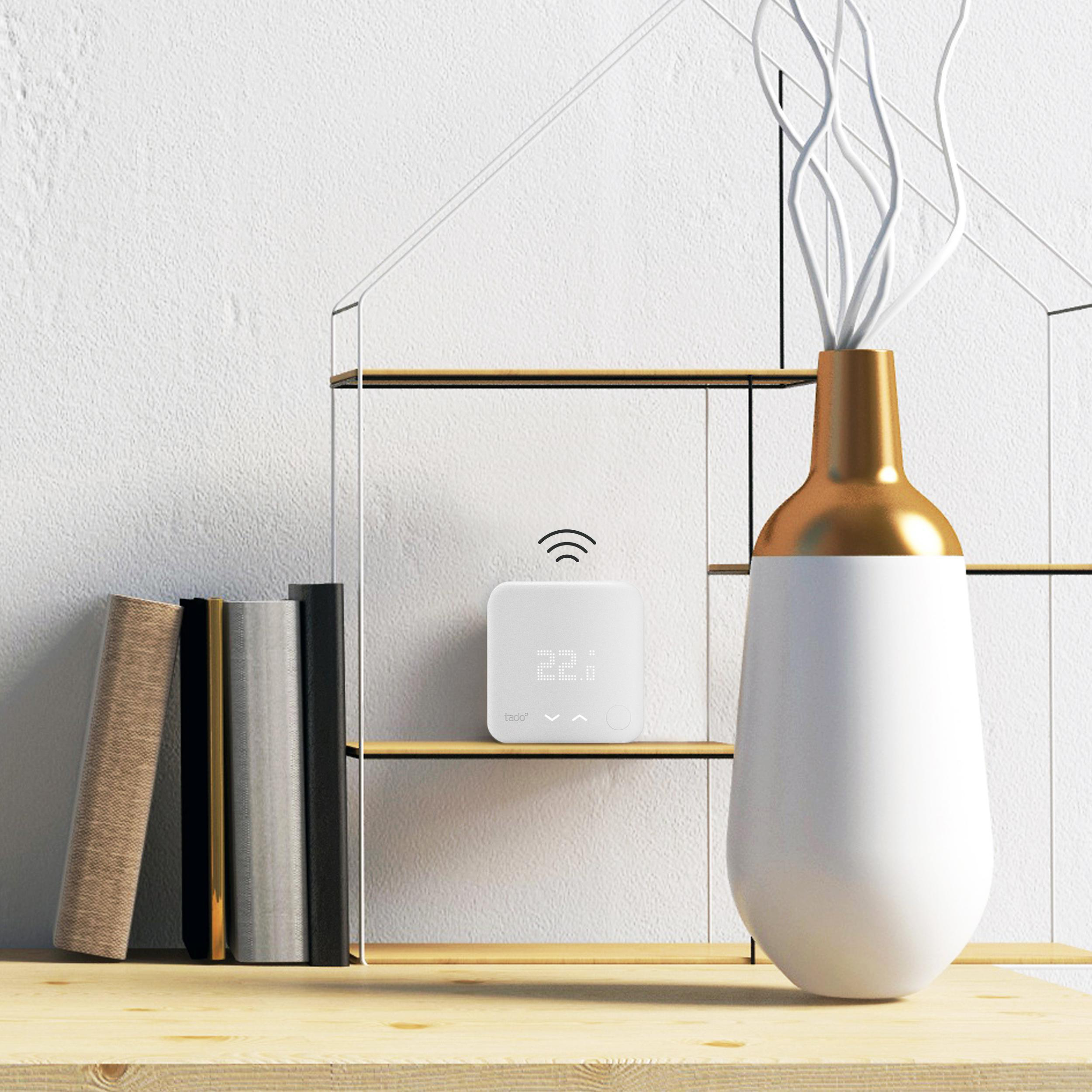 Ein Thermostat mit digitaler Anzeige, neben Büchern und einer Vase.