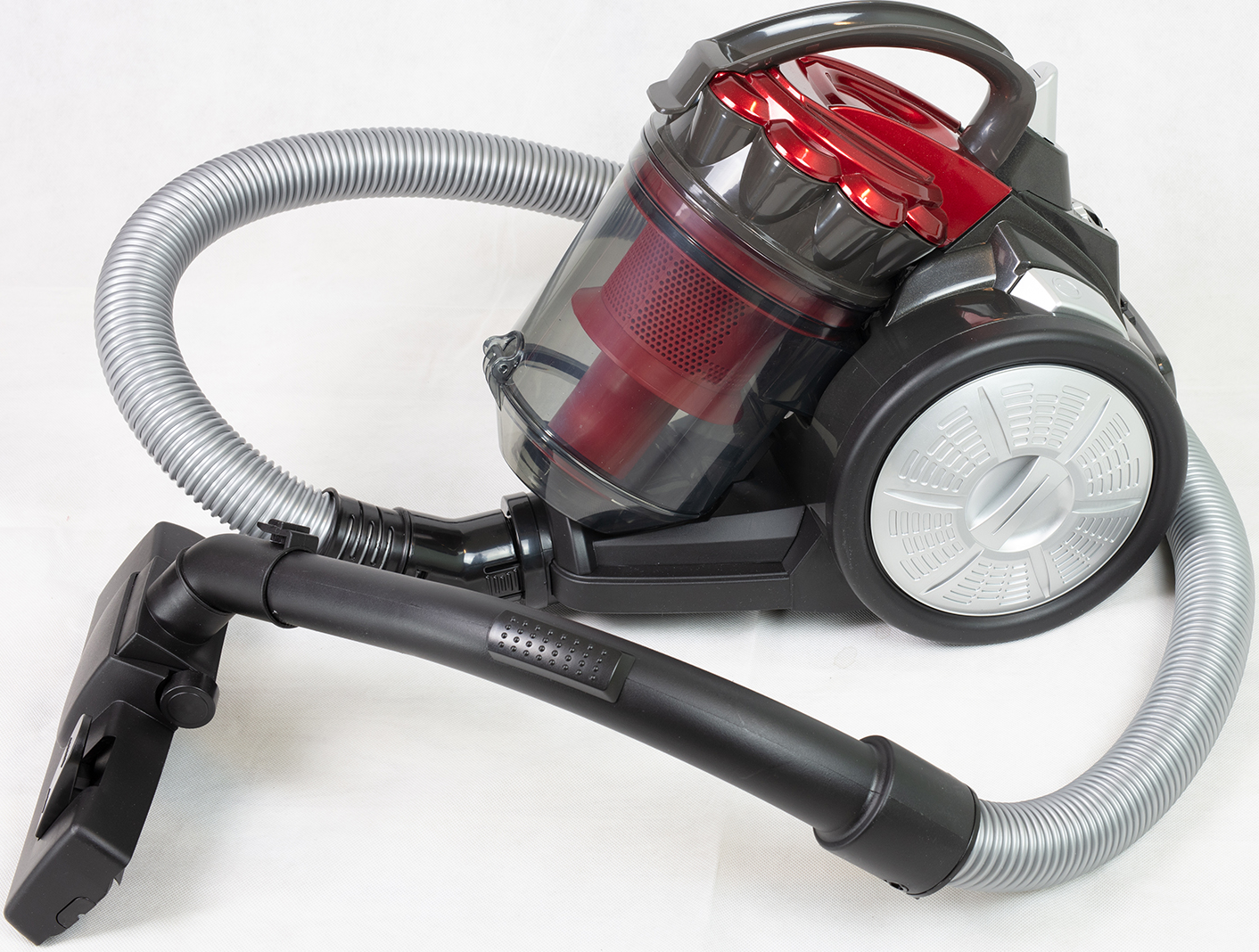 Un aspirateur noir et rouge avec un tuyau et une brosse argentés, le tout sur une surface blanche.