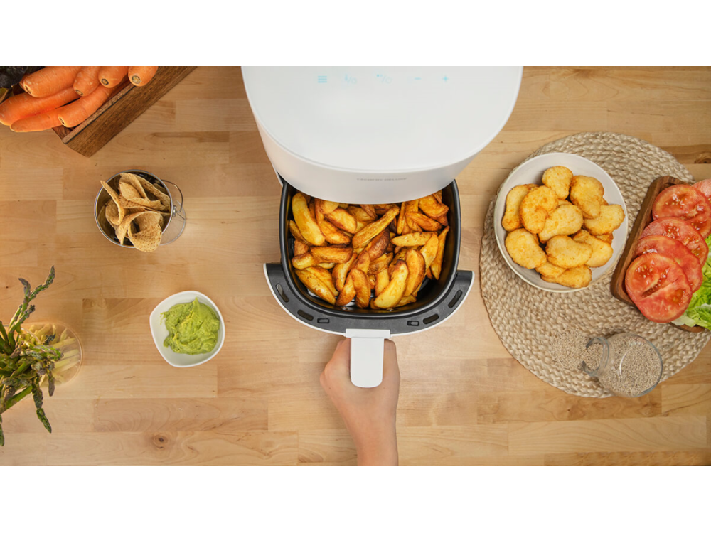 Vista cenital: Freidora de aire con papas fritas, nuggets, guacamole y otros alimentos en una mesa de madera.