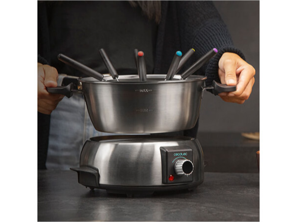 Un juego de fondue con olla y tenedores, manos de una persona sosteniendo la olla.