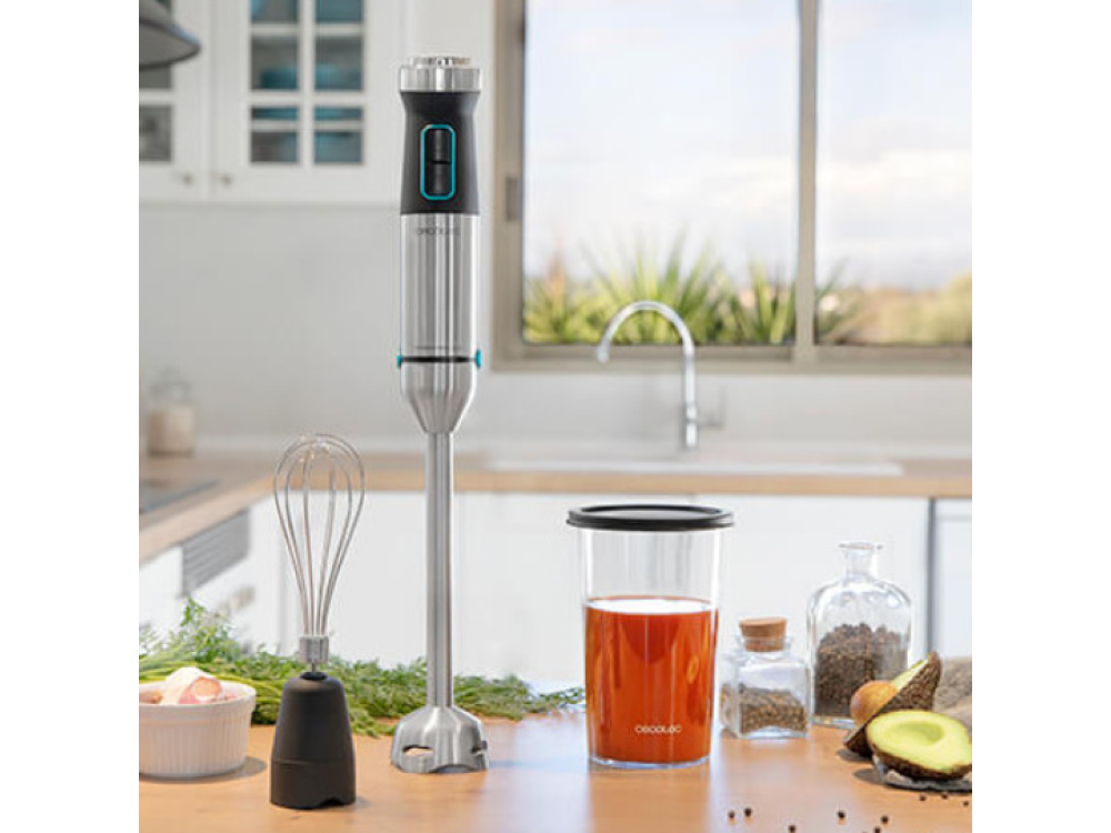 Batidora de mano con accesorios junto a un vaso de jugo e ingredientes frescos.