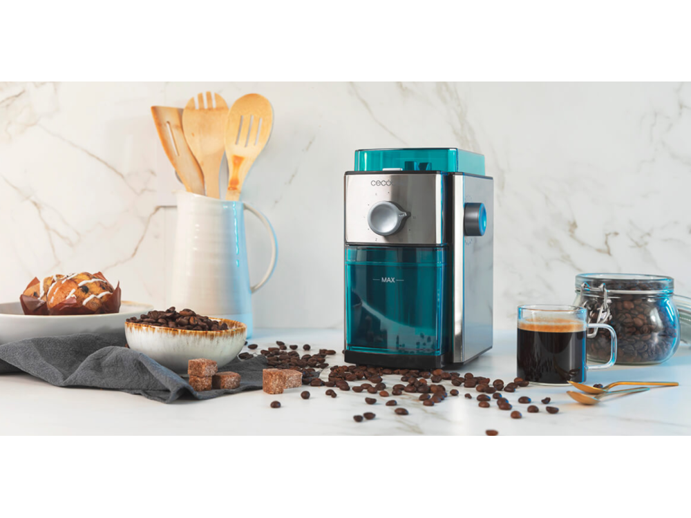 Molinillo de café con granos de café, pasteles y una taza de café en una mesa.