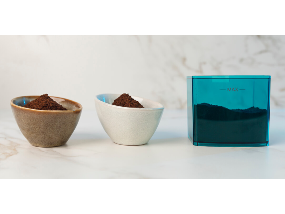 Tres cuencos con posos de café y un recipiente azul sobre una superficie blanca.