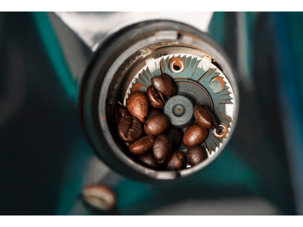 Primer plano de granos de café en un molinillo. Granos marrones, partes grises del molinillo.