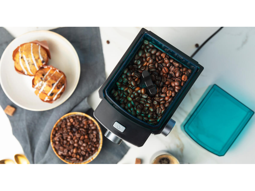 Granos de café y un molinillo, magdalenas y una tapa azul.