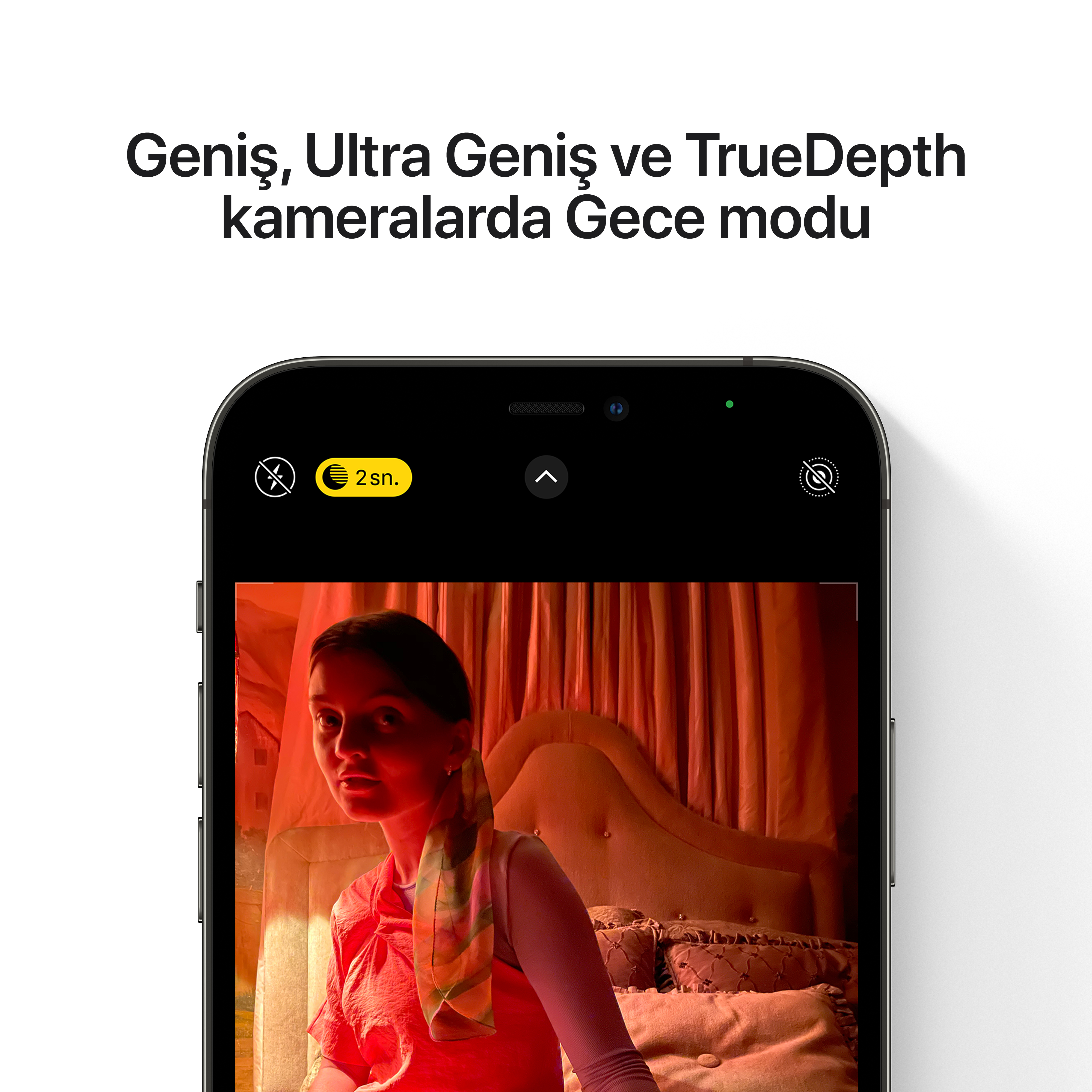 Bir odada bir kadının yüzünü gösteren iPhone ekranı. Gece modu açık ve metin ultra geniş kamera diyor.
