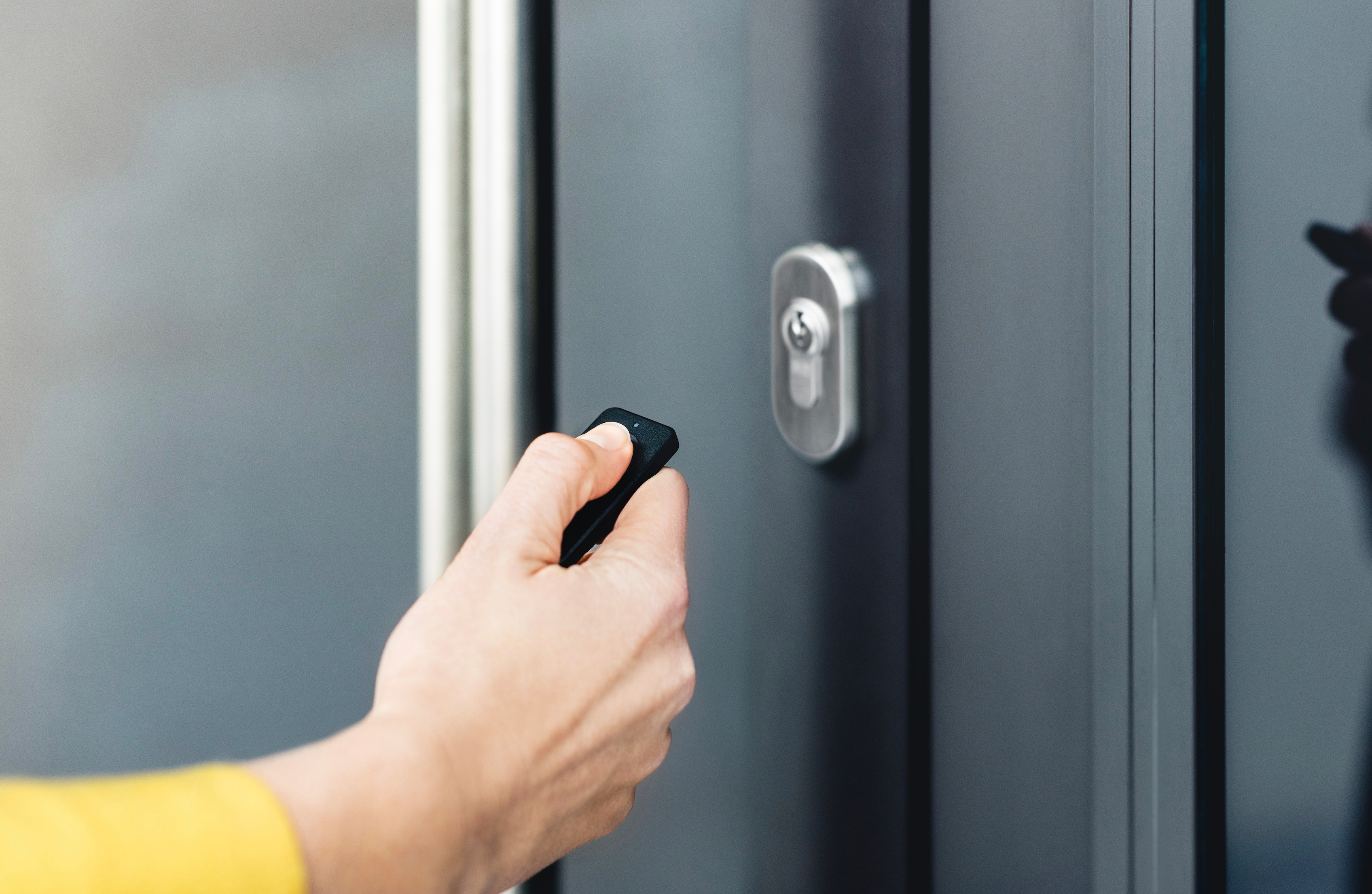 Una mano che tiene un portachiavi nero vicino a una porta grigia chiusa con una serratura.