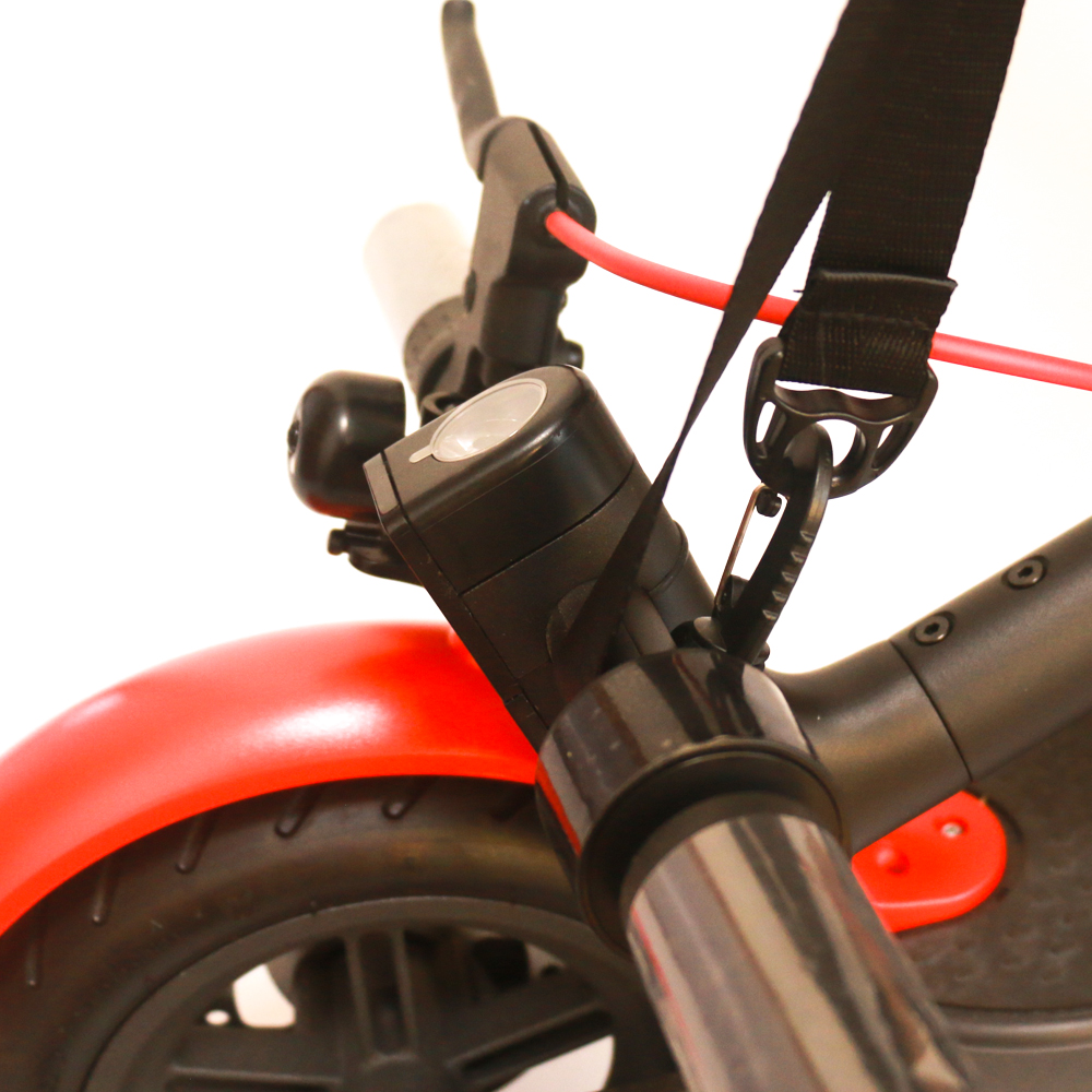 Primer plano del manillar del scooter. Muestra luz, timbre y fijación de correa. Scooter rojo.