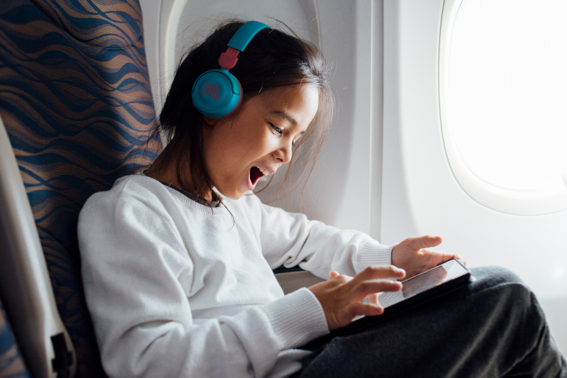 A child on a plane, wearing headphones and using a tablet.
