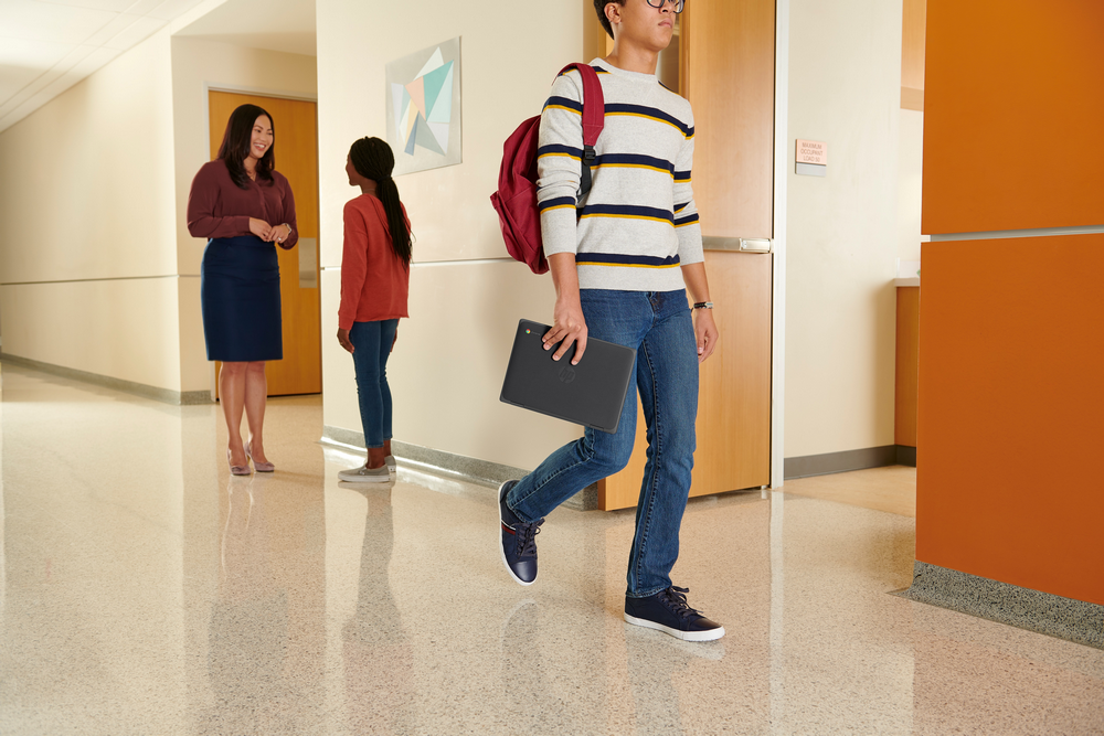 Estudiantes caminando por un pasillo escolar con una profesora.