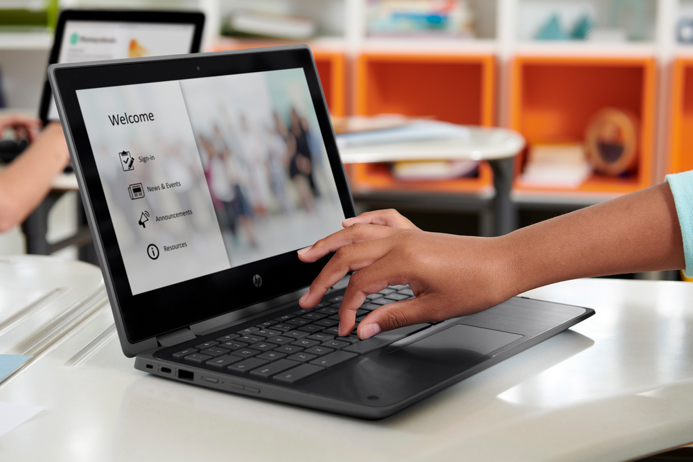 Una persona usa una laptop con una pantalla de bienvenida. Hay opciones de inicio de sesión, noticias y recursos.