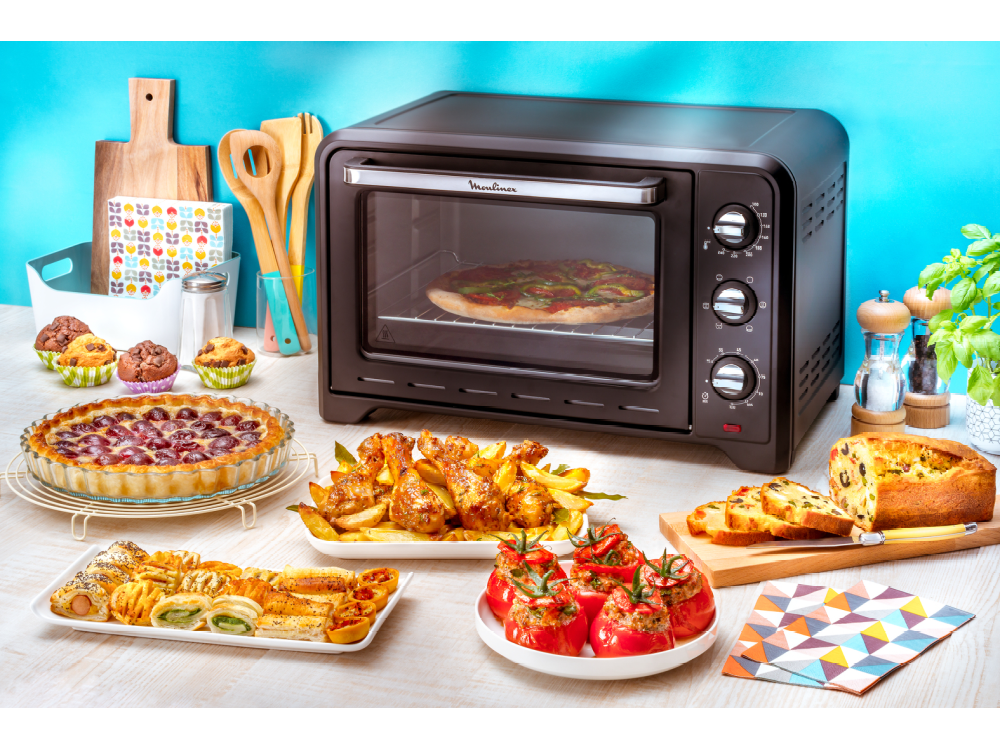 Un horno negro con pizza, pasteles y otros platos sobre una mesa. Fondo azul.