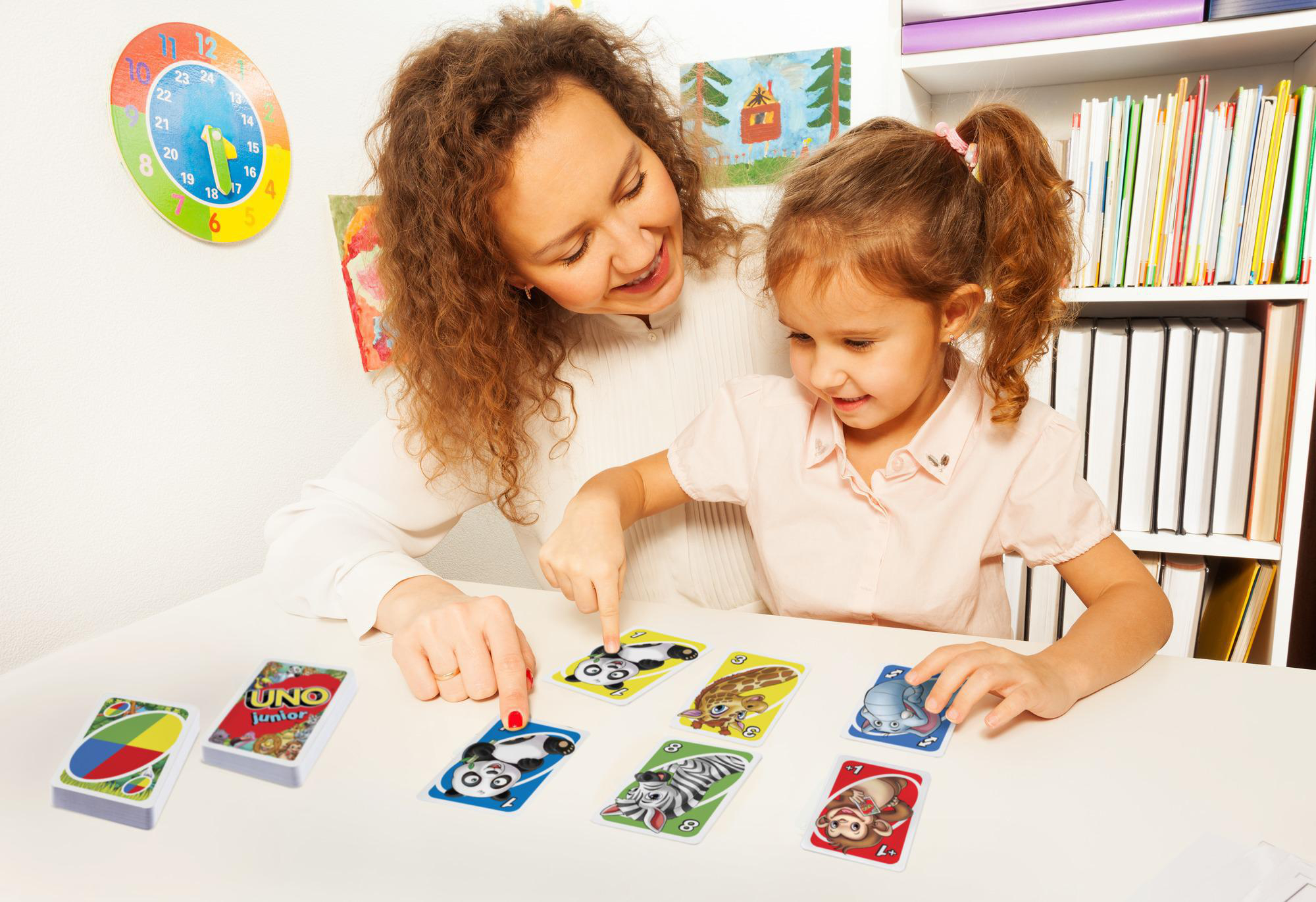 Mutter und Tochter spielen Uno. Die Mutter zeigt auf eine Karte. Verschiedene Karten liegen auf dem Tisch.