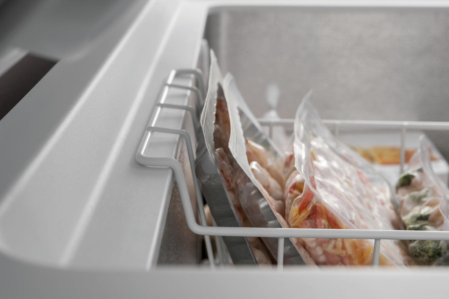Ein Gefrierschrank mit Packungen gefrorener Lebensmittel im Inneren. Es gibt ein weißes Gestell, das die Packungen hält.