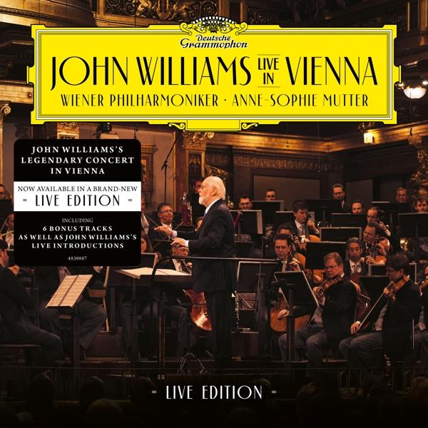 John Williams Live in Vienna Albumcover. Ein Dirigent leitet ein Orchester. Menschen im Publikum. Gelber Hintergrund.