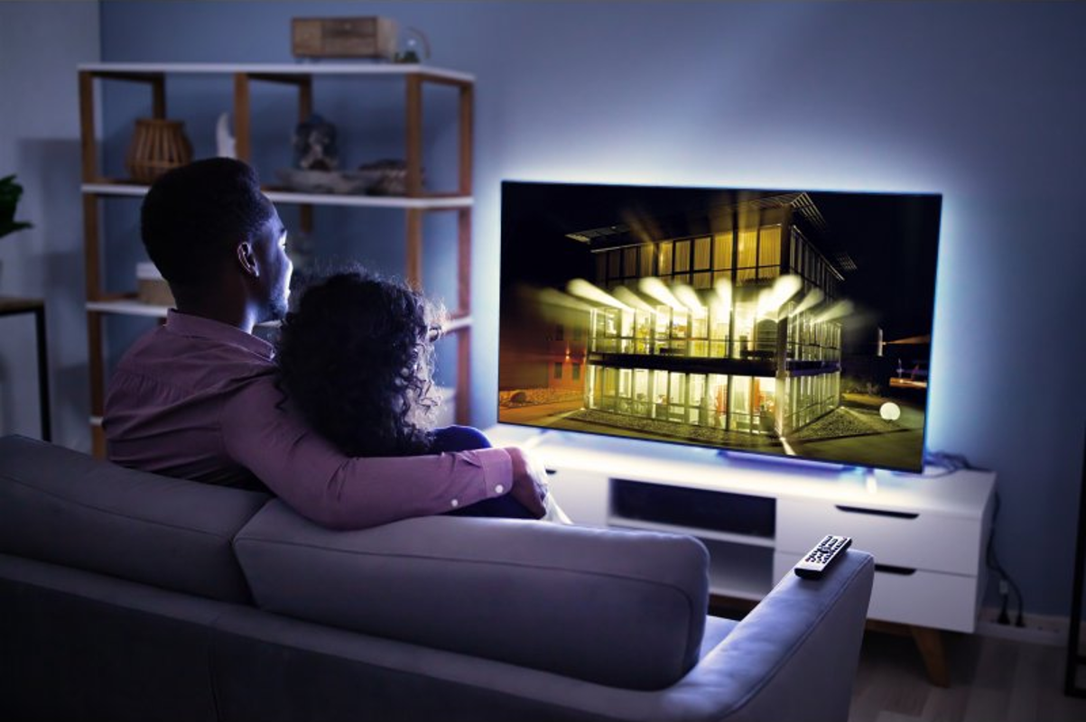 Coppia che guarda la TV in un soggiorno moderno. La TV mostra una casa moderna e luminosa.