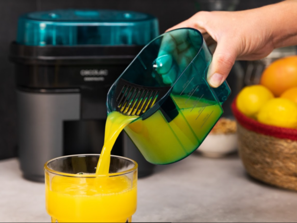 Jugo vertiéndose de una jarra verde a un vaso. Exprimidor en el fondo.