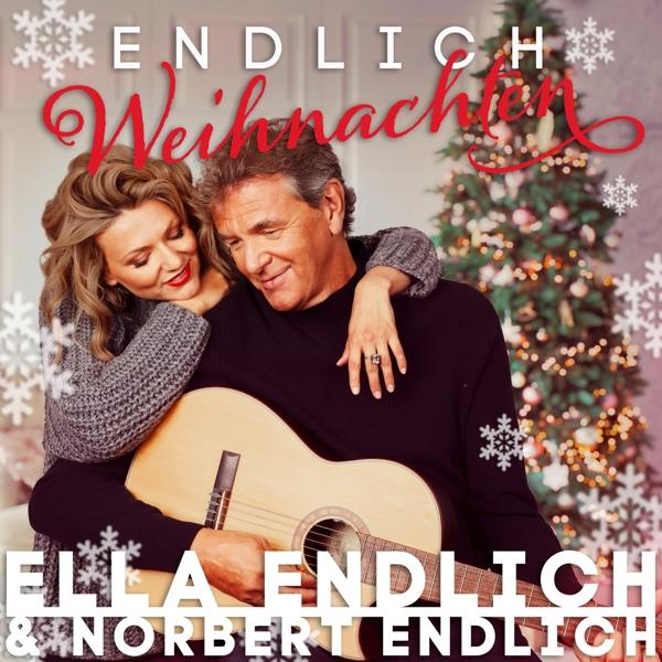 Ein Paar umarmt sich, ein Mann hält eine Gitarre, mit Weihnachtsdekorationen.