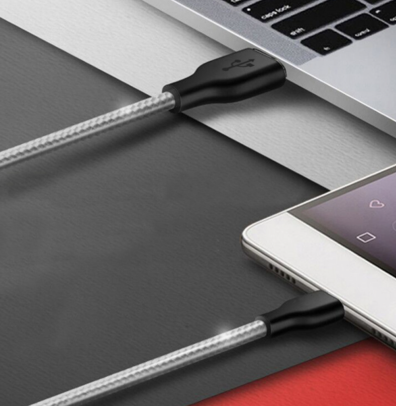 Egy ezüst-fekete USB-kábel telefonhoz és laptophoz csatlakozik. A kábelen USB-csatlakozó van.