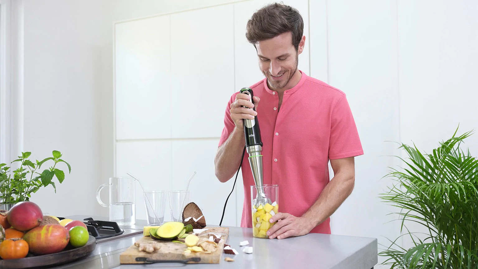 Homme utilisant un mixeur plongeant pour mélanger des fruits jaunes dans un verre.