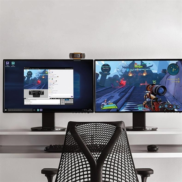 Two computer monitors displaying a game and a video call, with a webcam on top.