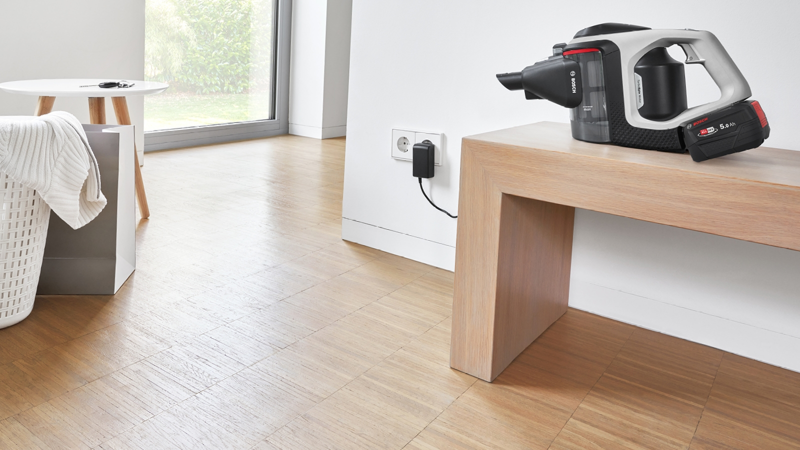 Kabelloser Staubsauger auf einer Holzbank, wird geladen. An eine Steckdose angeschlossen, Holzboden.