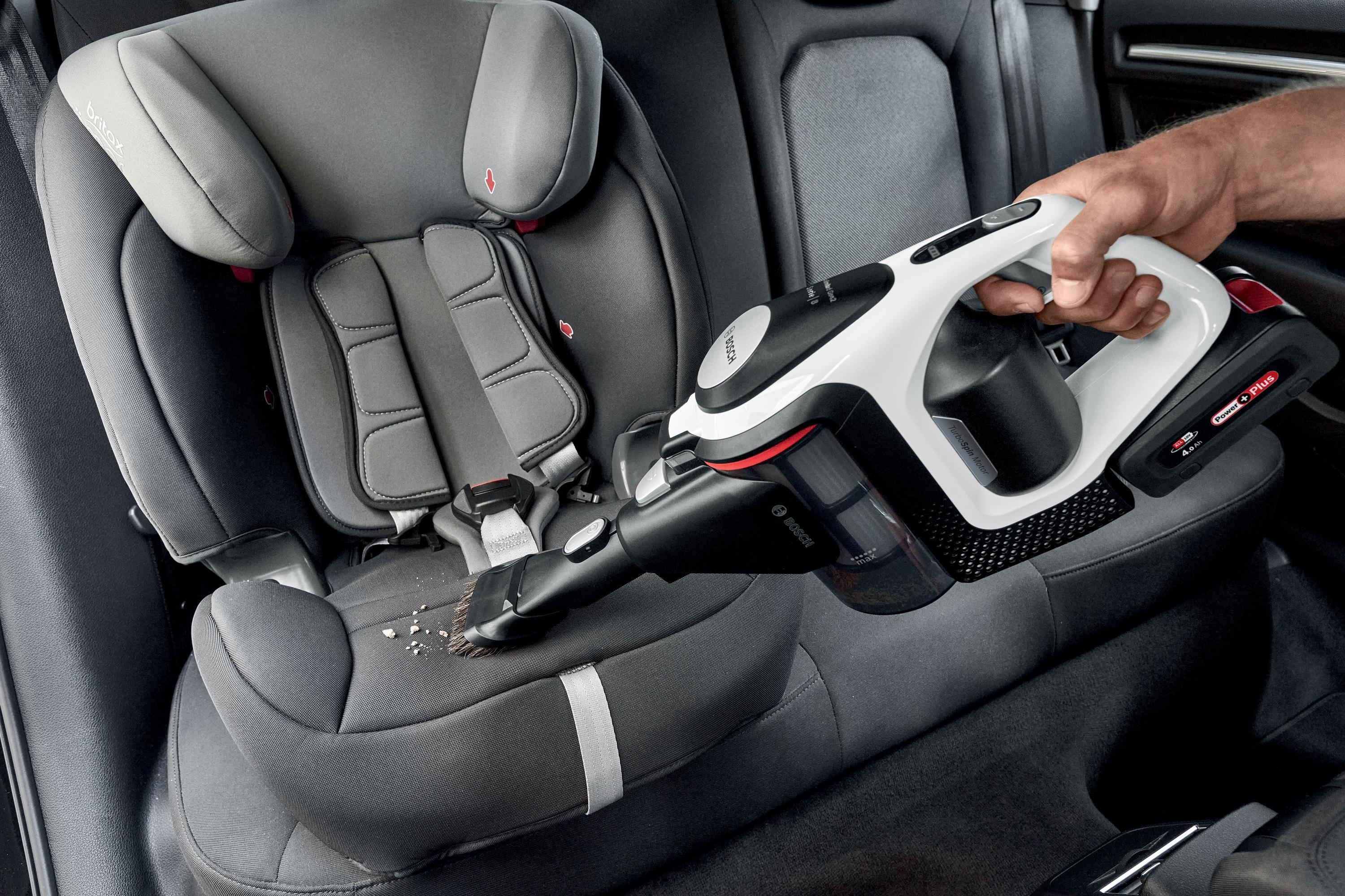 Eine Hand, die einen Autositz mit einem Handstaubsauger absaugt.