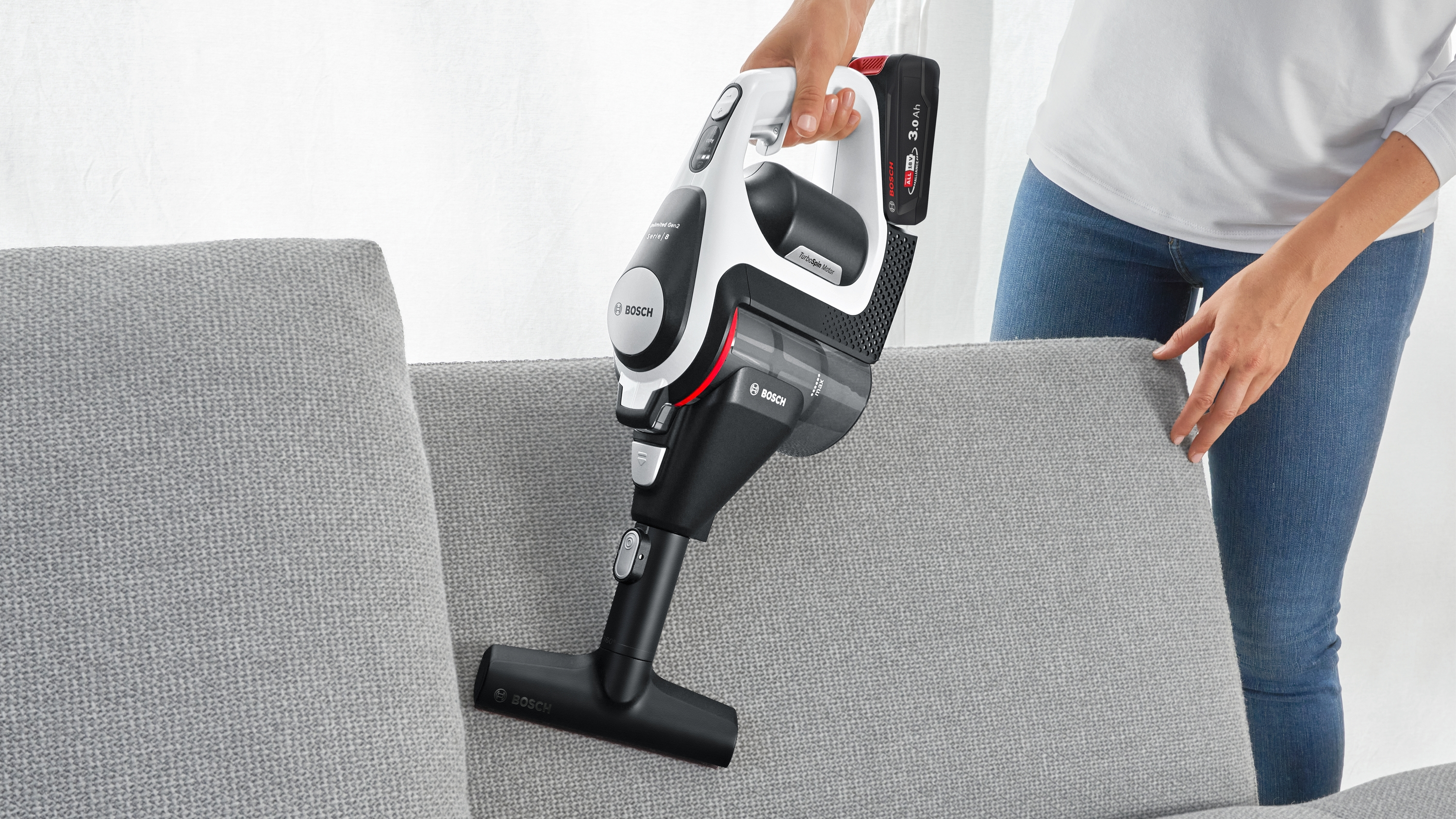Frau, die einen Sofa absaugt. Ein schwarz-weißer Staubsauger und ein graues Sofa.
