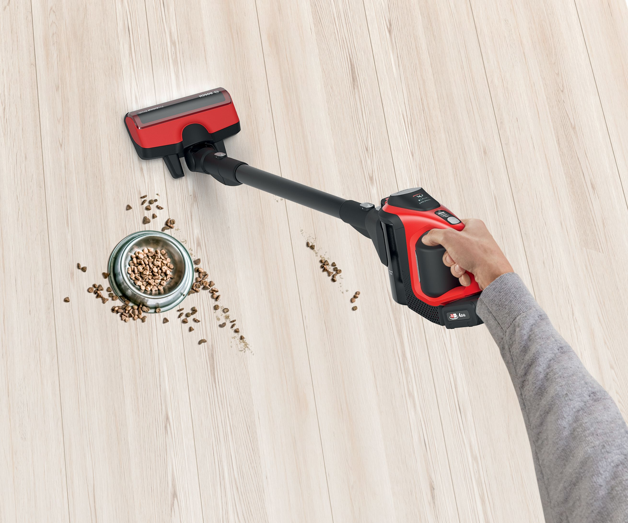 Eine Person reinigt verschüttetes Tierfutter mit einem kabellosen Staubsauger.