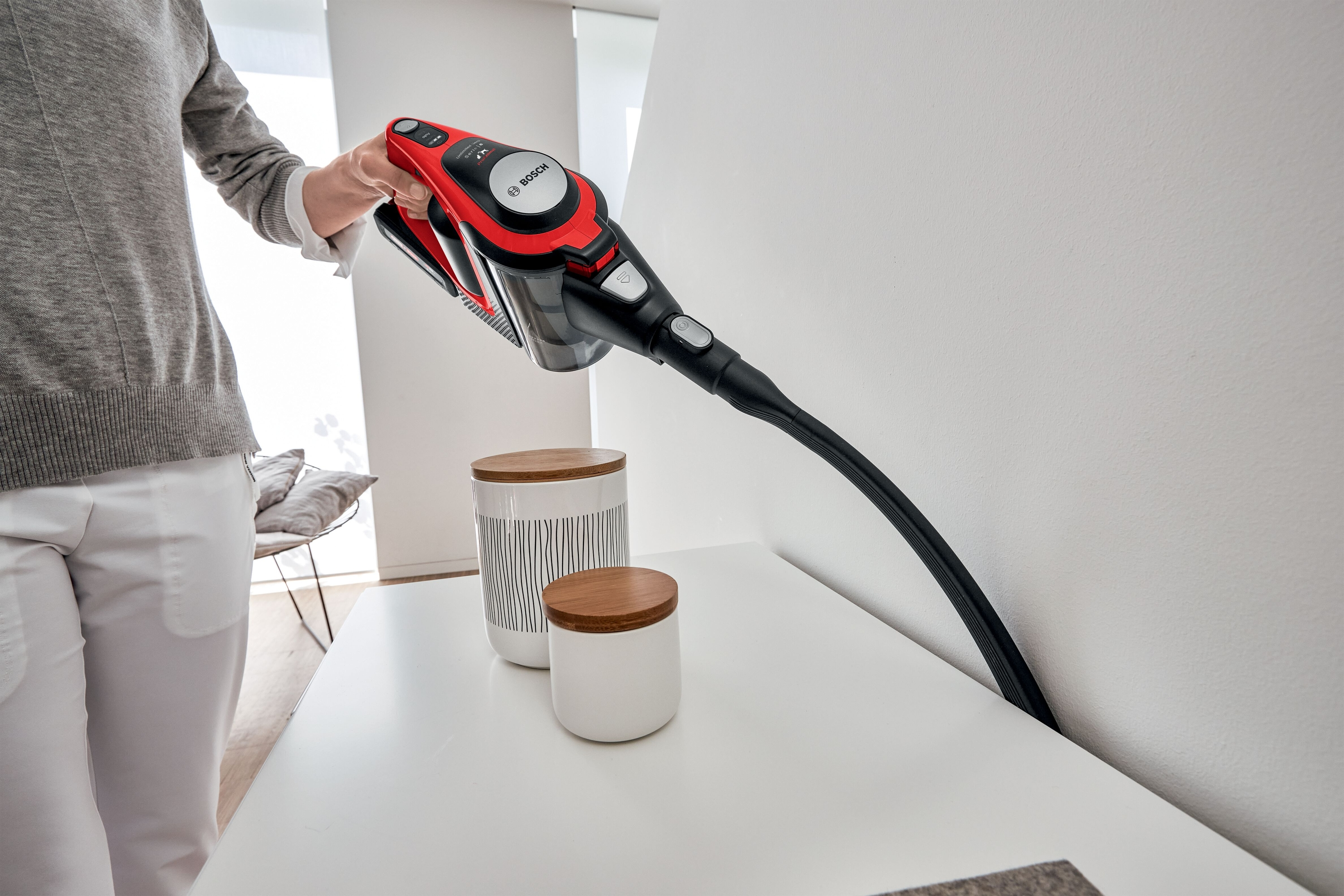 Person verwendet einen rot-schwarzen Staubsauger, um die Kante eines weißen Tisches zu reinigen.