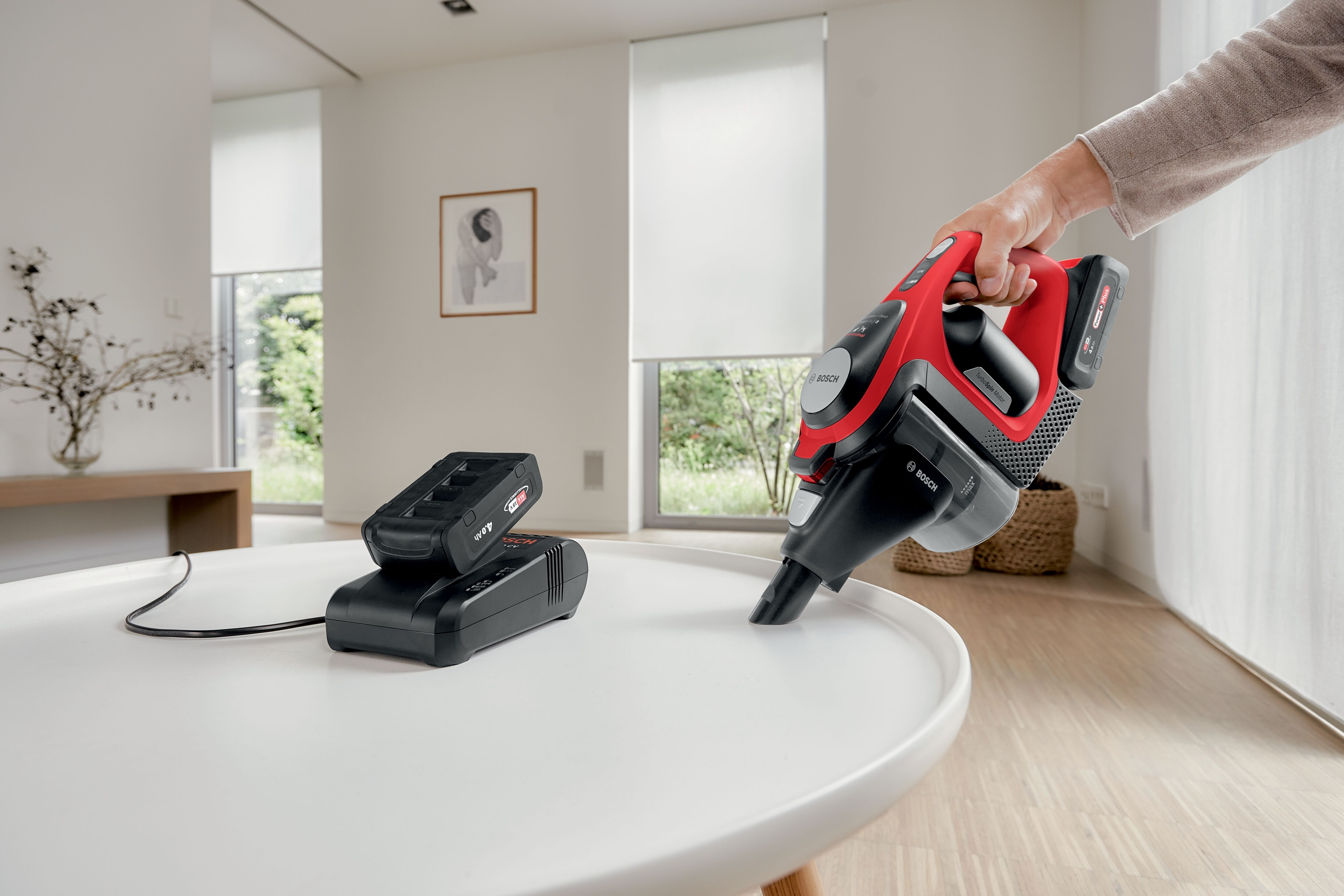 Eine Person benutzt einen rot-schwarzen Bosch Staubsauger auf einem weißen Tisch.