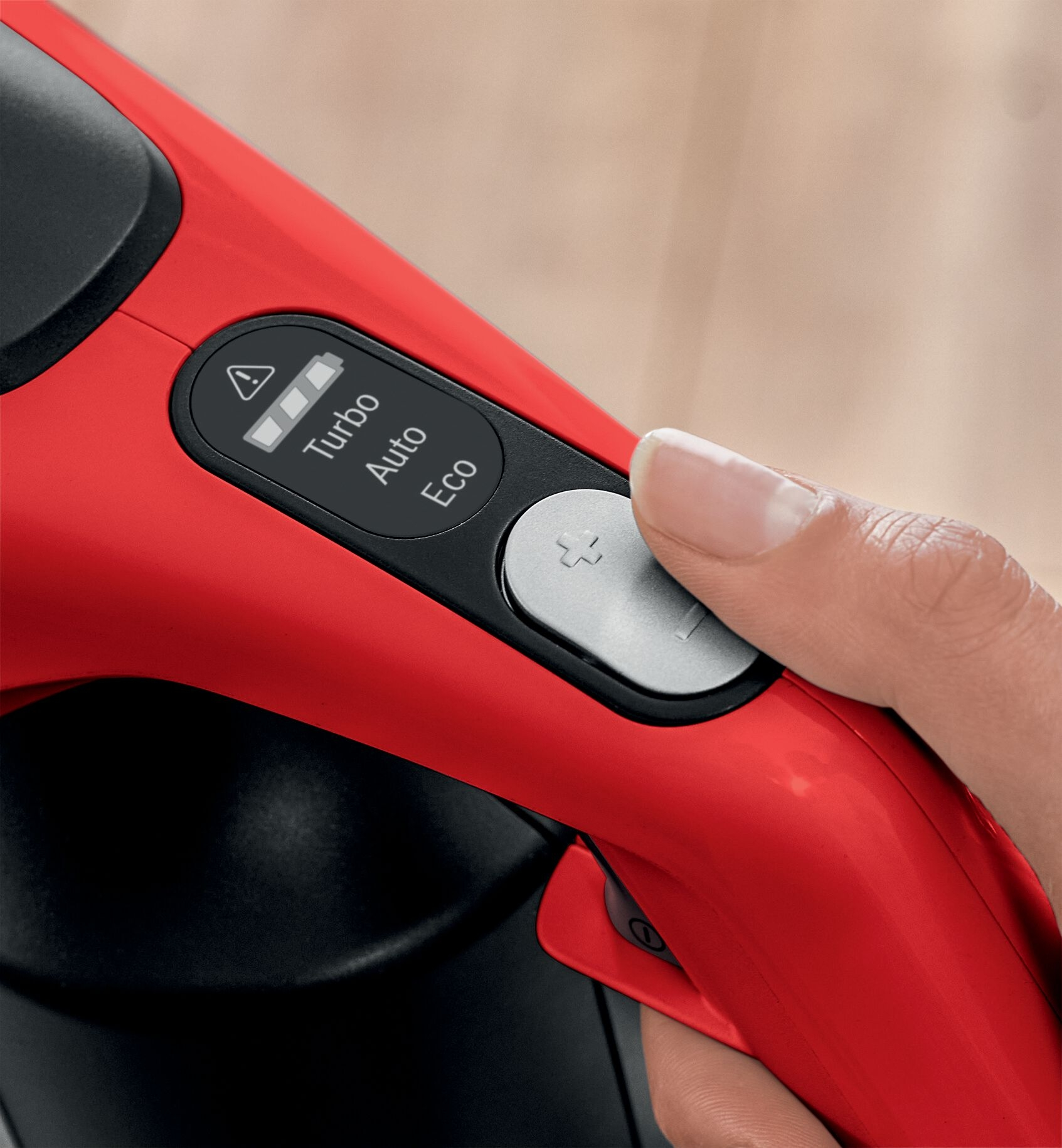 Die Hand einer Person drückt eine Taste an einem roten Staubsauger.