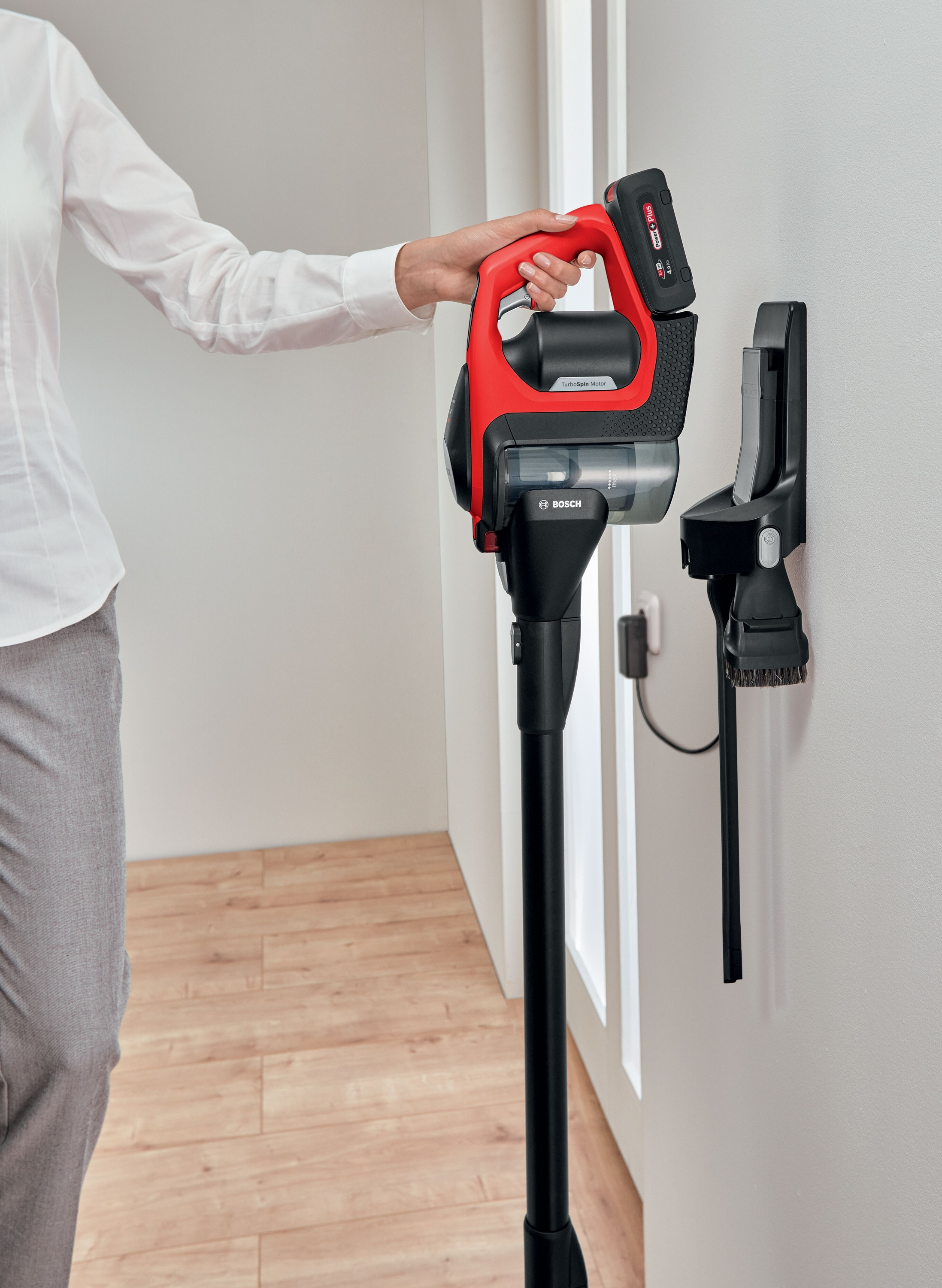 Frau benutzt einen rot-schwarzen kabellosen Staubsauger an der Wand.