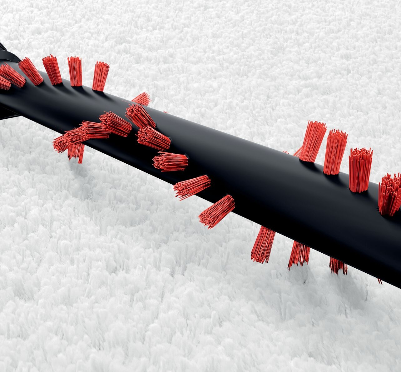 Ein schwarzer Staubsaugerbürstenkopf mit roten Borsten ist auf einem weißen Teppich abgebildet.