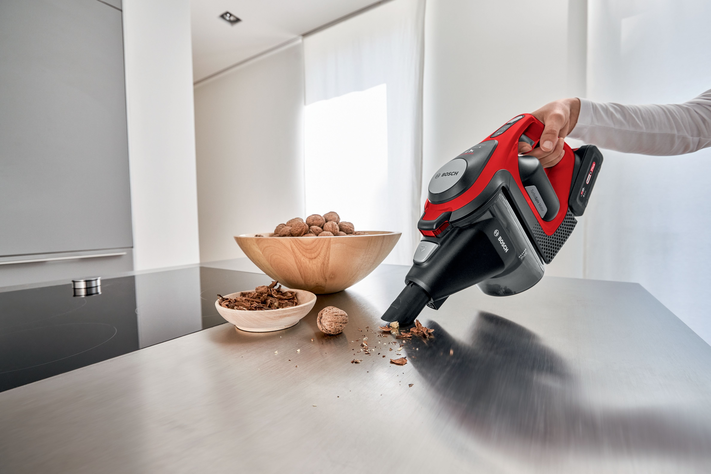 Person verwendet einen rot-schwarzen Bosch-Handstaubsauger auf einer Arbeitsplatte.