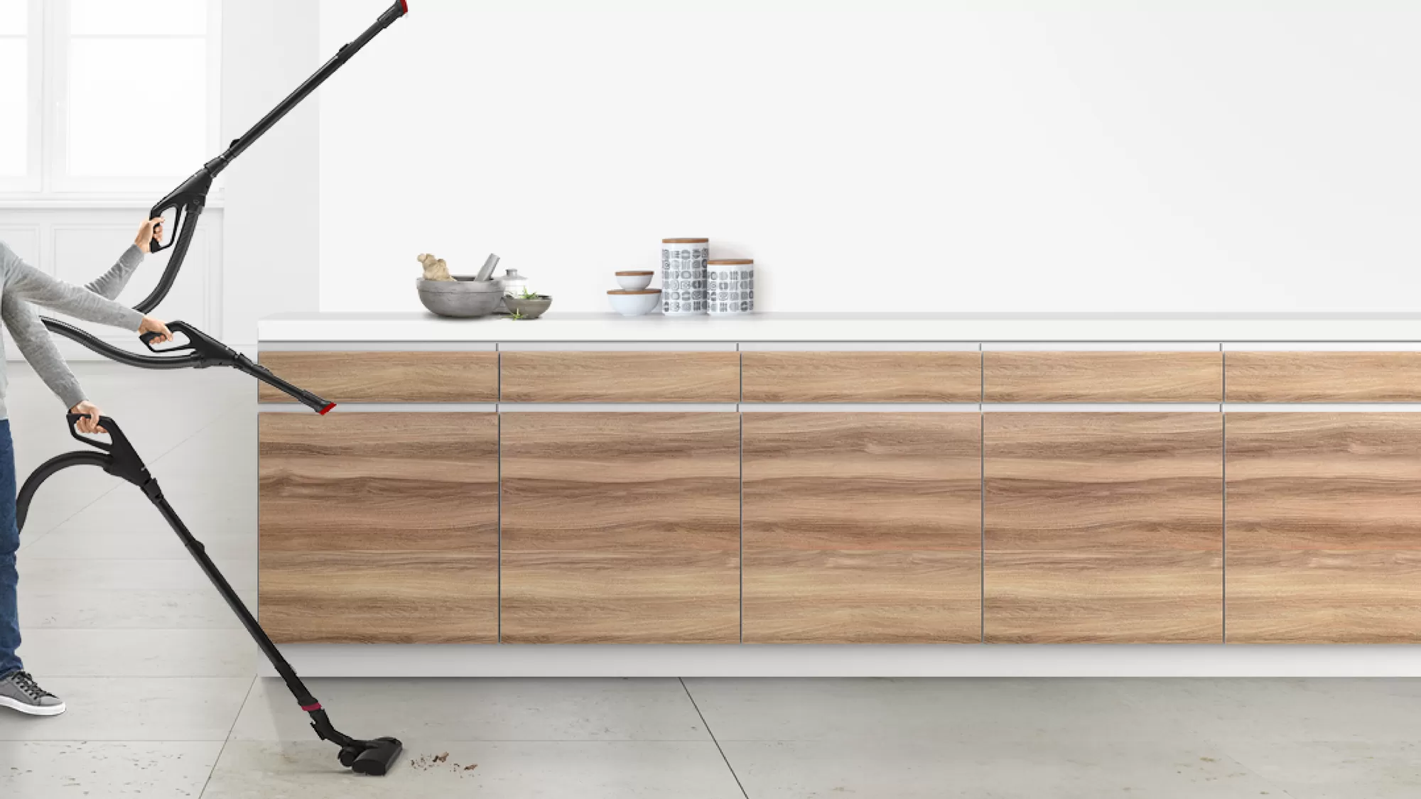 Person, die einen Staubsauger benutzt. Holzschrank, weiße Arbeitsplatte und Fliesenboden sichtbar.