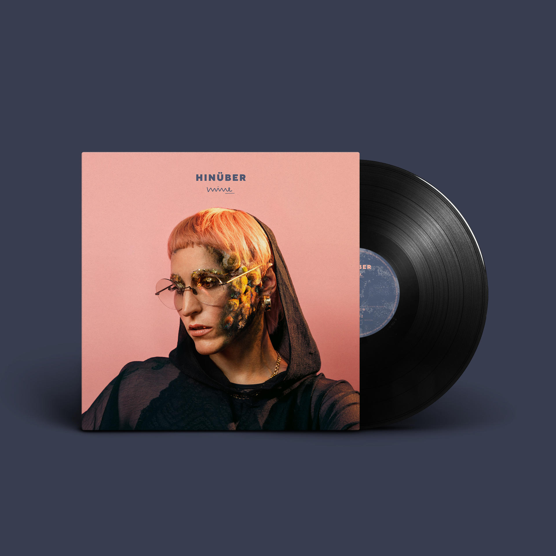 Albumcover zeigt Person mit pinken Haaren, Brille und schwarzem Hoodie, daneben eine Schallplatte.