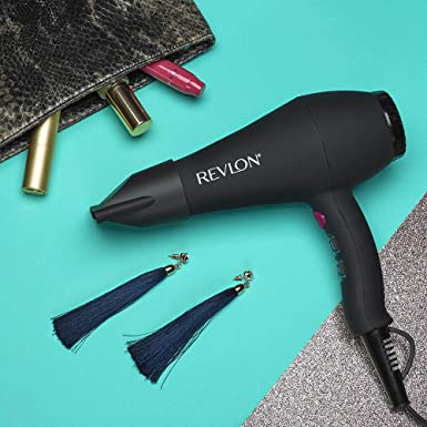 Schwarzer Haartrockner, Make-up-Tasche und marineblaue Quastenohrringe auf türkisfarbener Oberfläche.