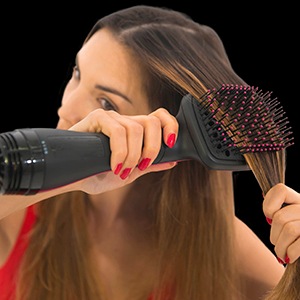 Eine Frau, die ihr Haar mit einer schwarz-rosa Haartrocknerbürste stylt und zur Seite schaut.
