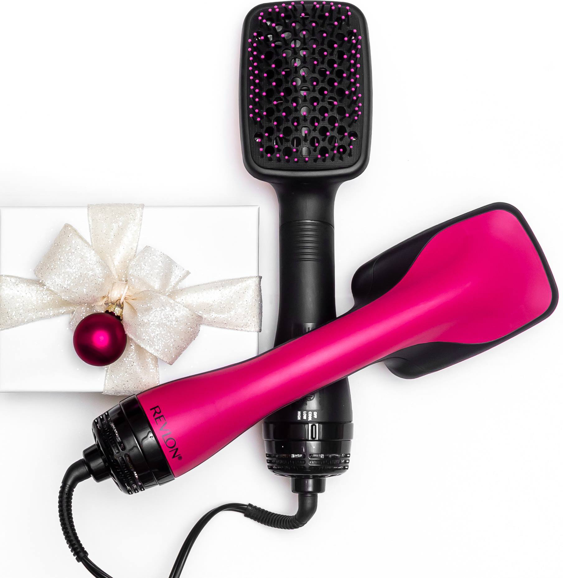 Ein pink-schwarzer Haartrockner mit einer weißen Geschenkbox und rotem Ornament auf weißem Grund.