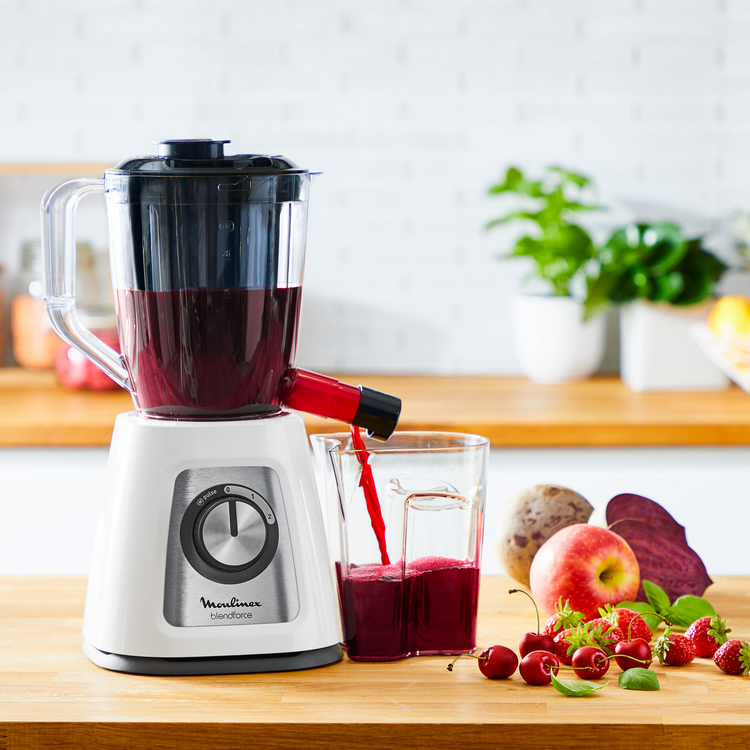 Una licuadora vierte jugo rojo en un vaso. Los ingredientes incluyen remolacha, manzana, fresas.