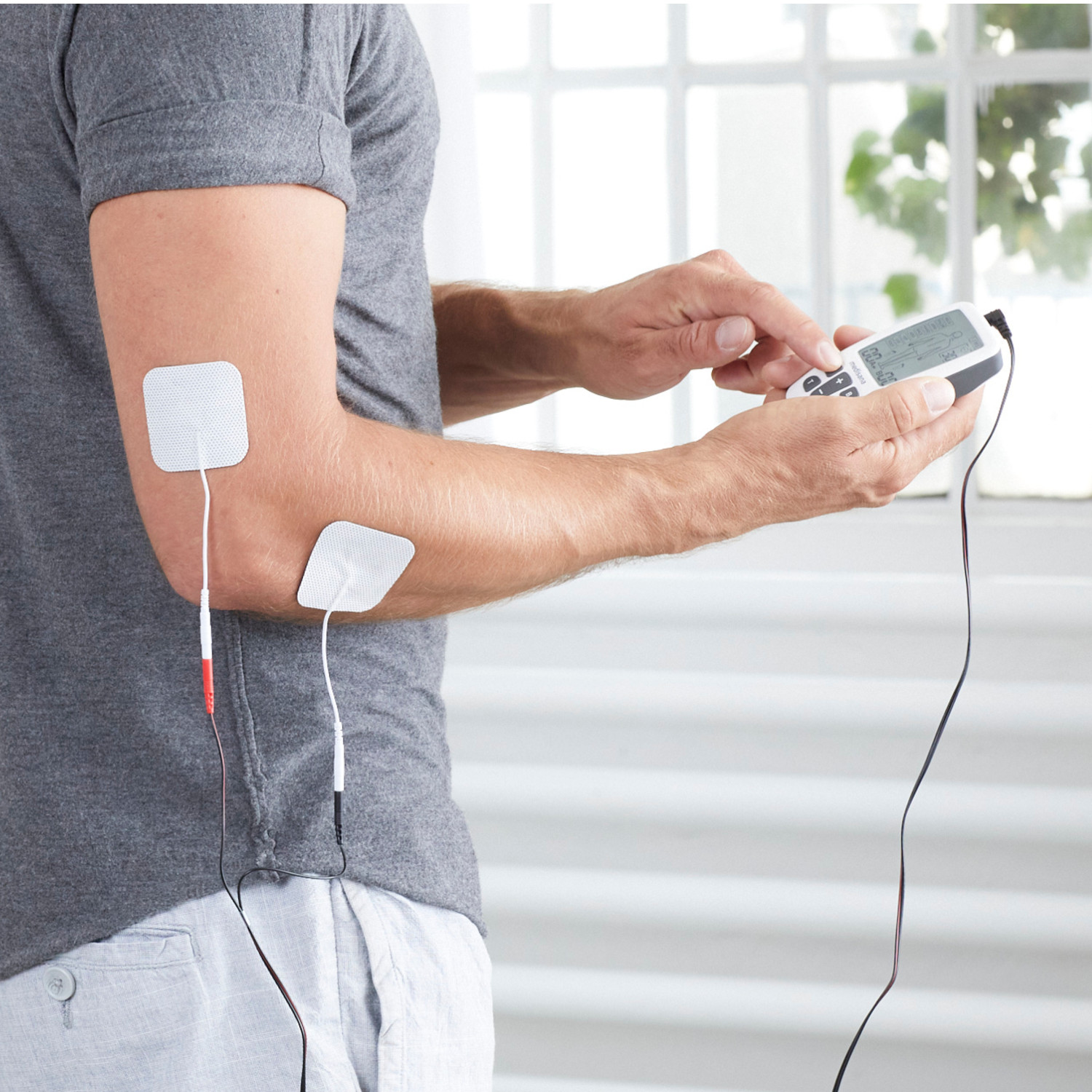 Person benutzt Gerät mit Pads am Arm zur Muskelstimulation.