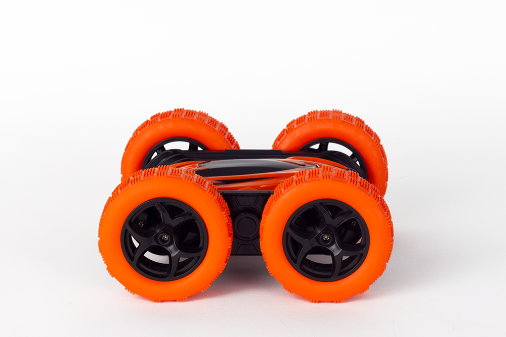 Orange and black toy car on white background. It has large orange wheels. The car is inverted.